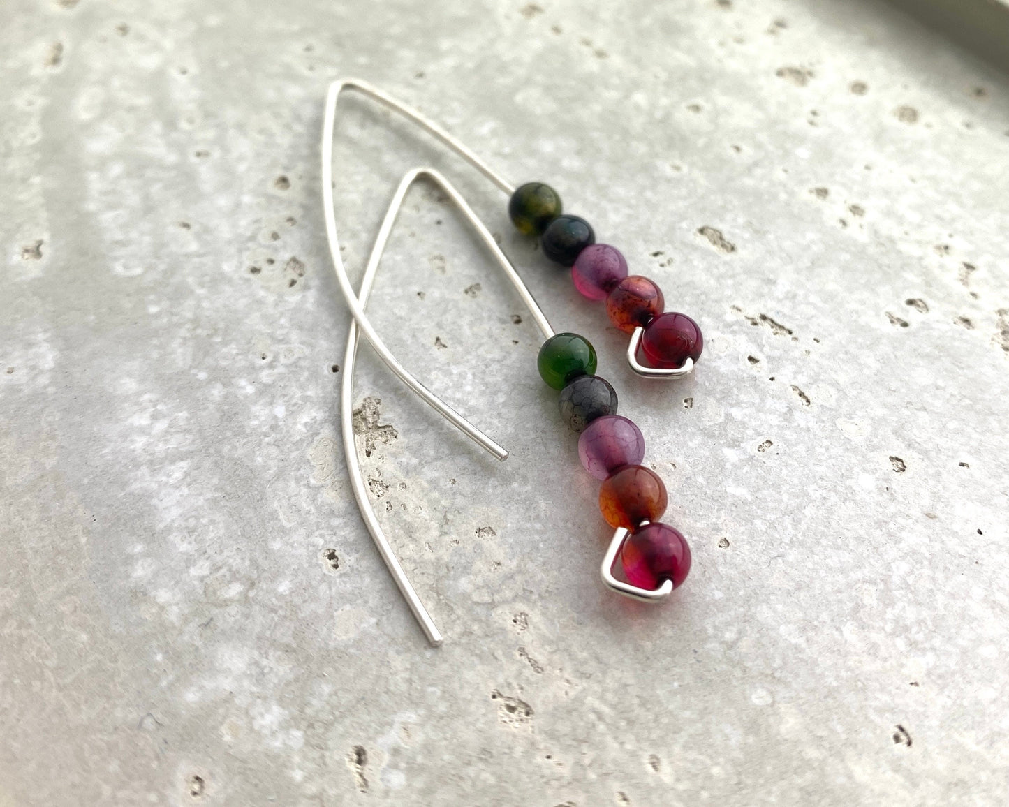 Silver earrings with multicolored beads on a light gray surface