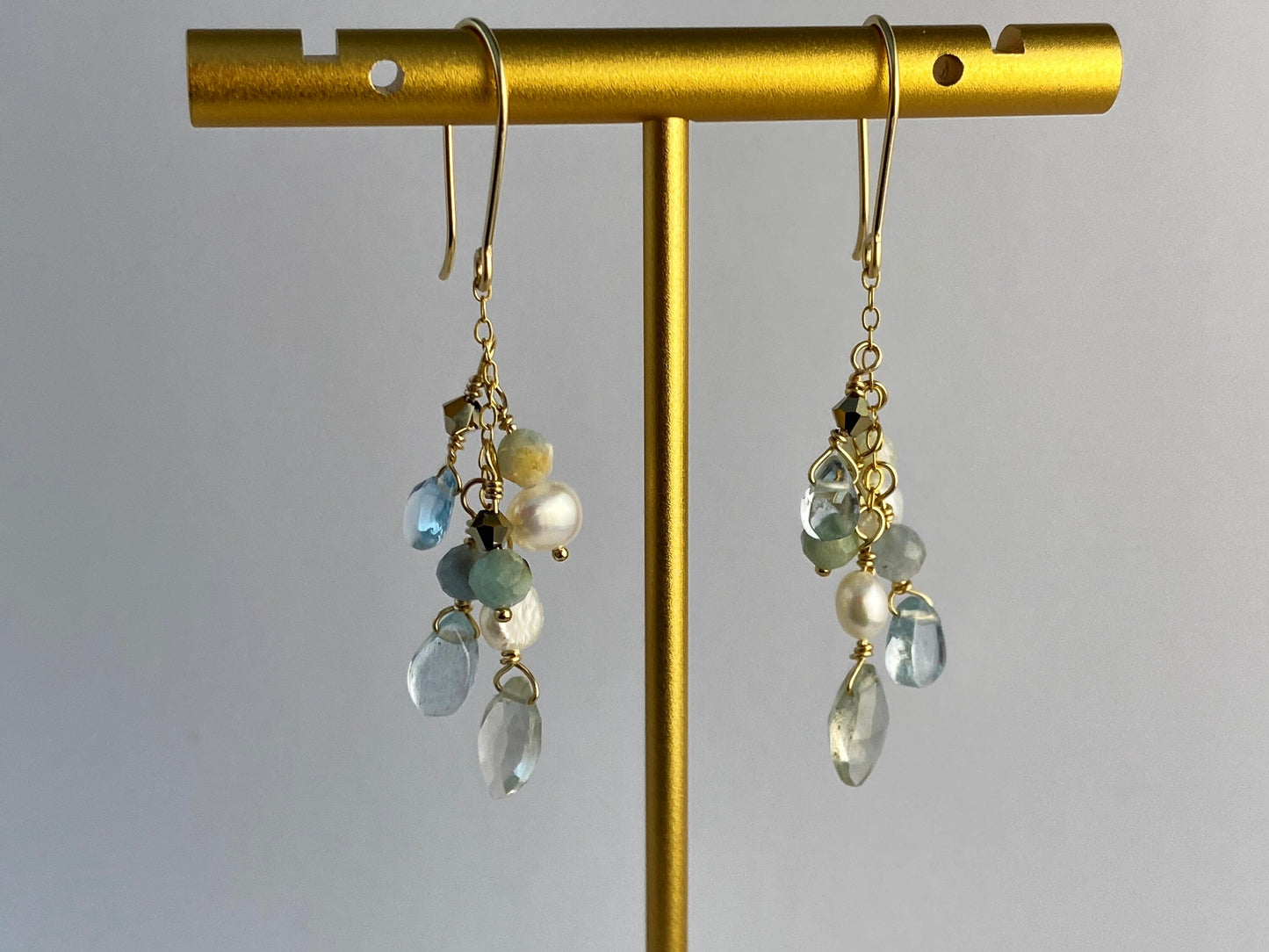 Gold earrings with gemstone drops on a gold stand against a gray background