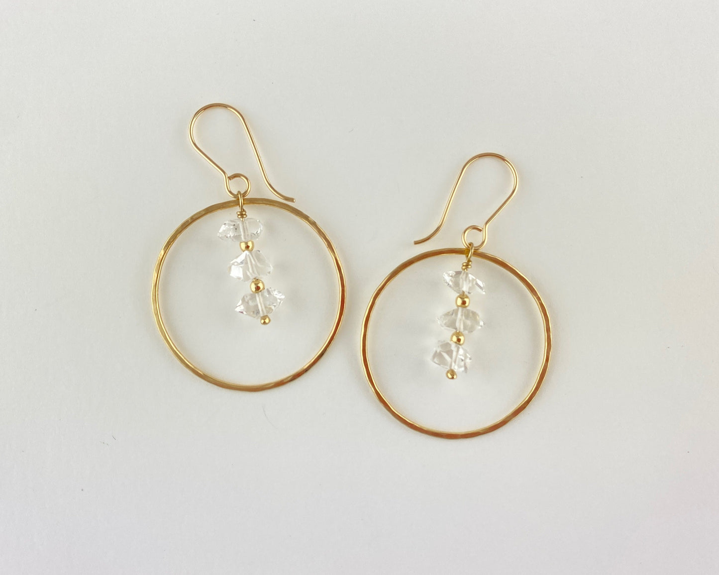 Gold hoop earrings with clear quartz beads on a light gray background