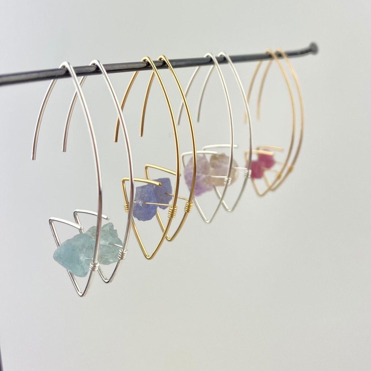 Gold and silver hoop earrings with embedded stones on a gray background