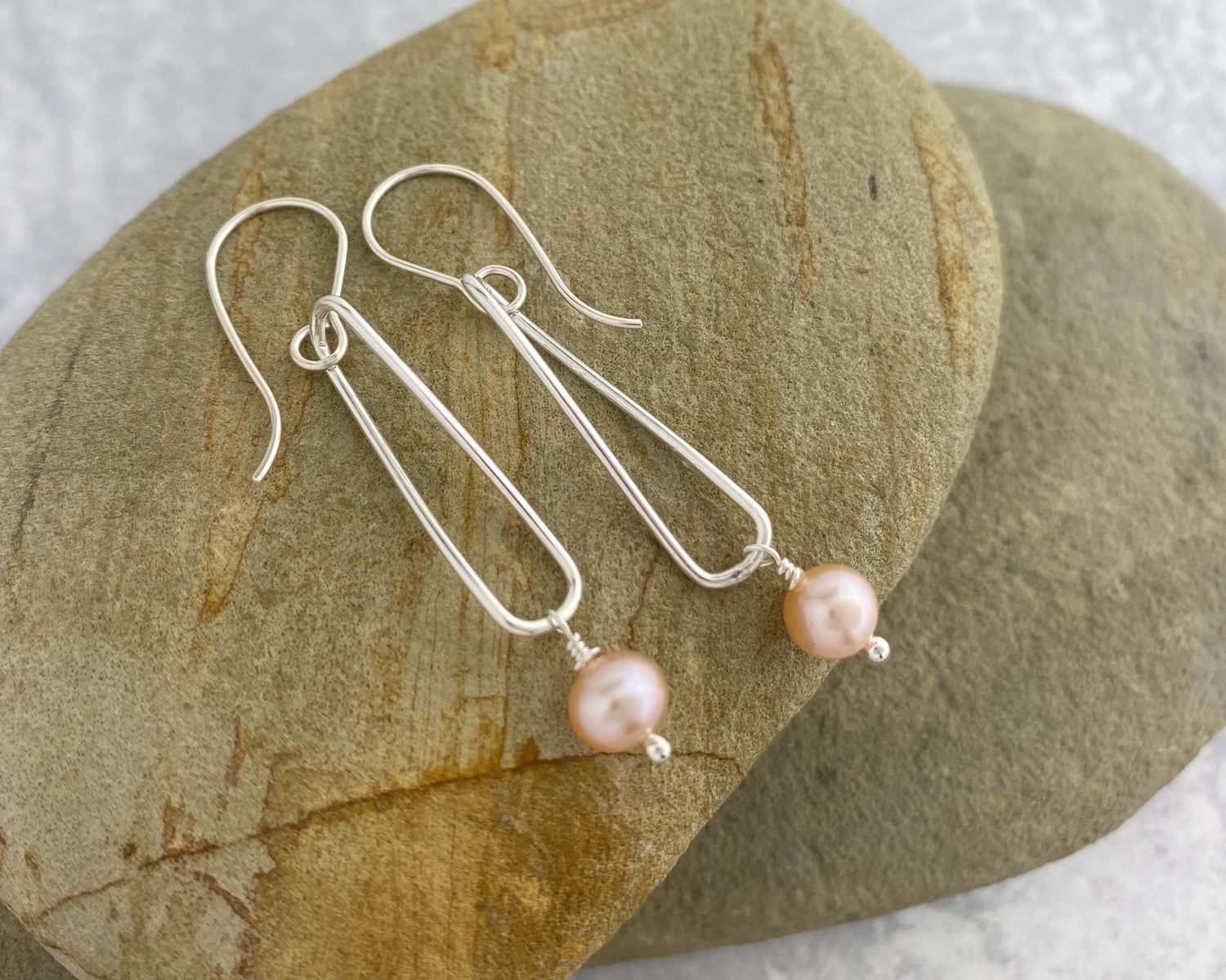 Round pink pearls dangle from twisted silver hoops