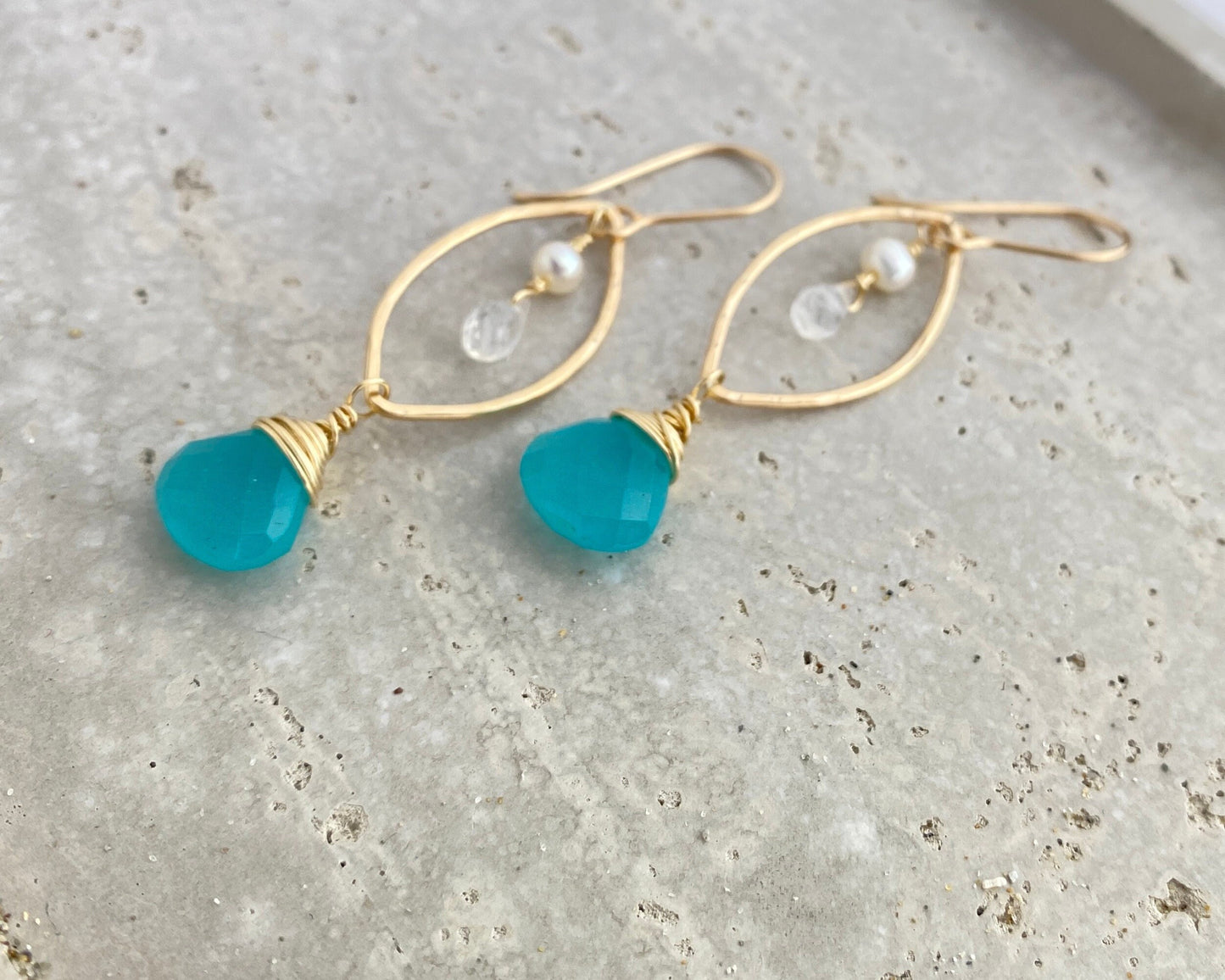 Gold earrings with blue beads on a textured surface