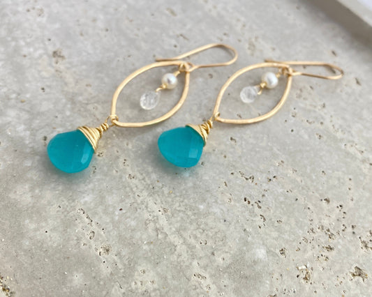 Gold earrings with blue beads on a textured surface