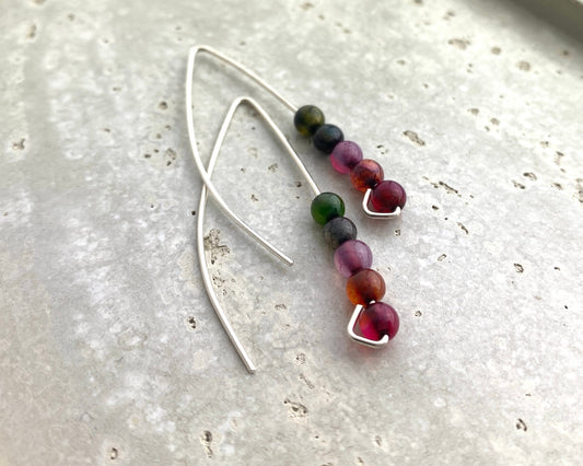 Silver earrings with multicolored beads on a light gray surface