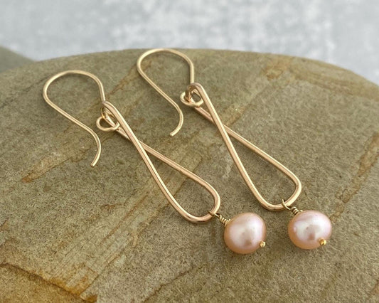 Gold earrings with pink pearls on a stone surface