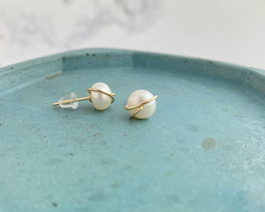 Pearl earrings with gold accents on a teal plate