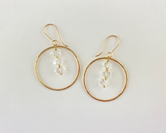 Gold hoop earrings with clear quartz beads on a light gray background
