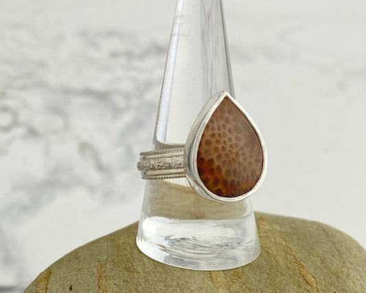 Ring with a teardrop-shaped brown stone on a clear stand with a blurred background