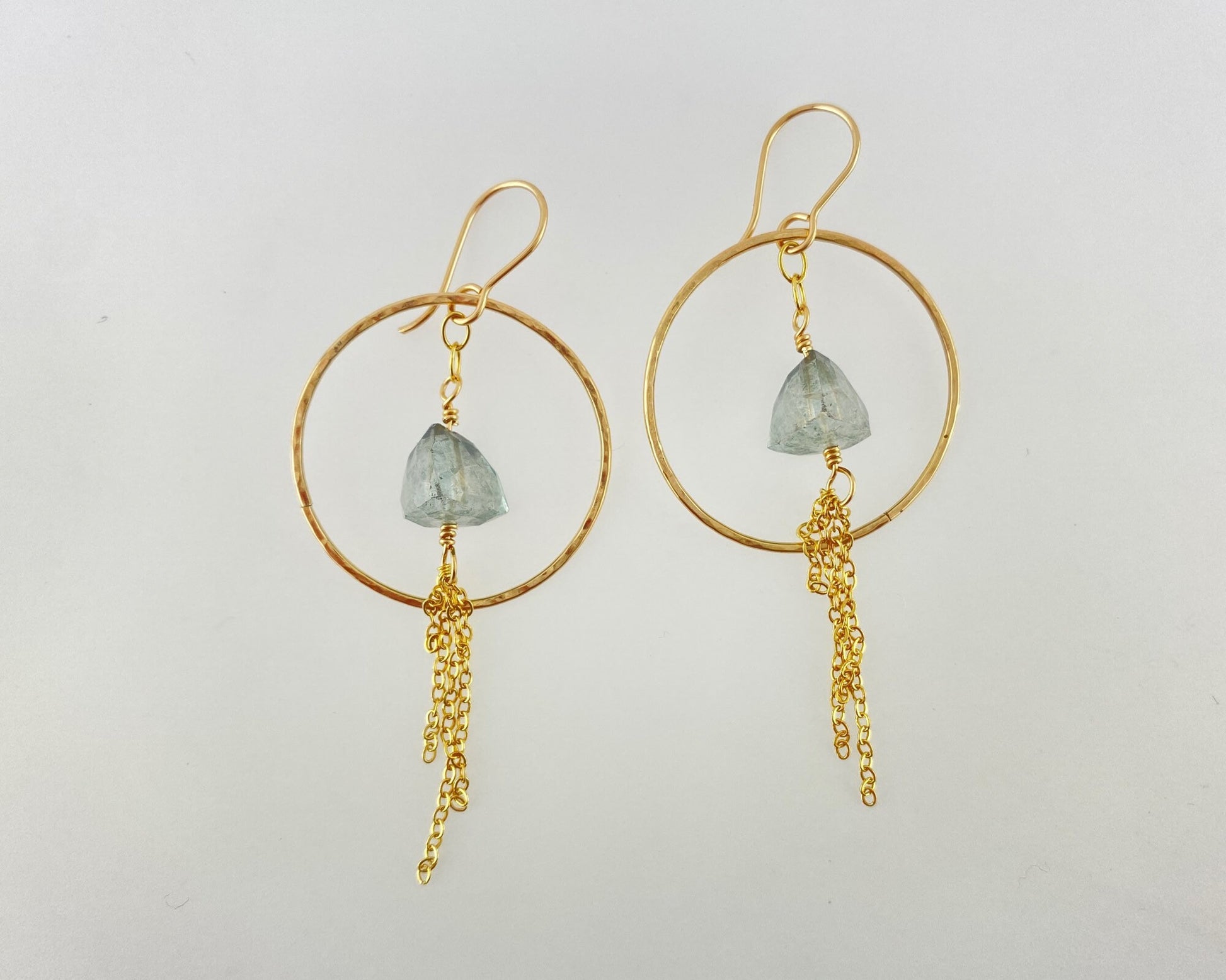 Gold hoop earrings with green gemstones and gold chains on a light gray background