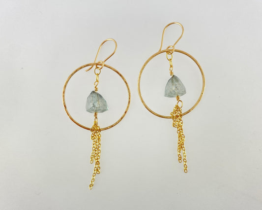 Gold hoop earrings with green gemstones and gold chains on a light gray background