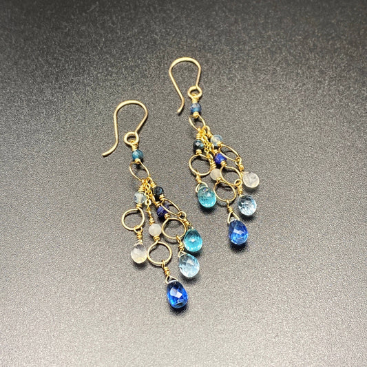 Gold earrings with blue and clear gemstones on a gray background