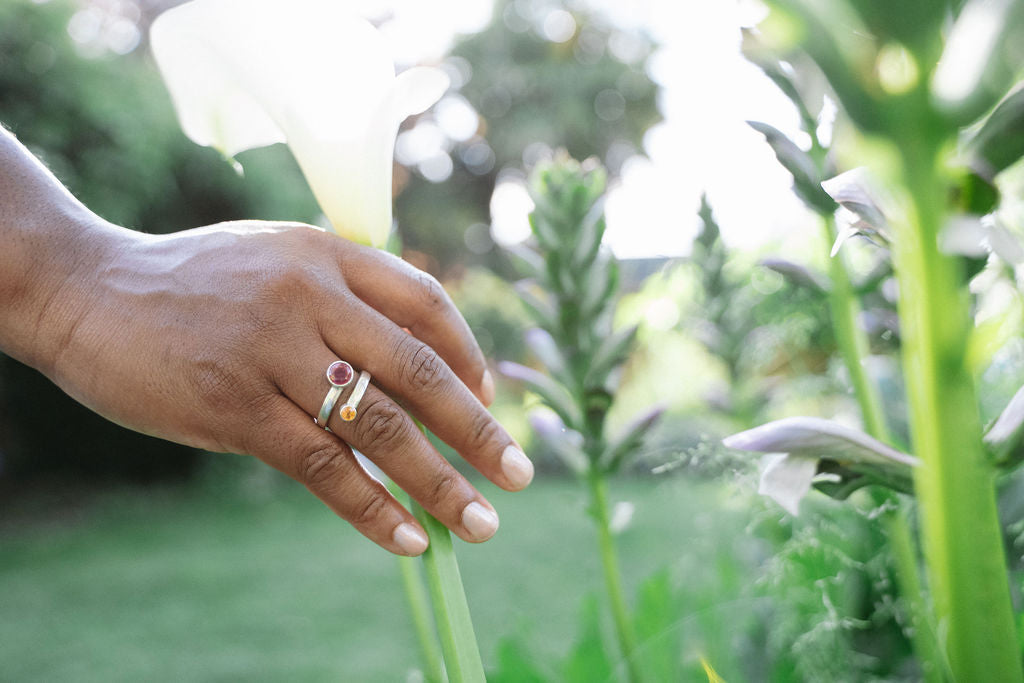 Hand with a ring holding a white flower in a garden setting