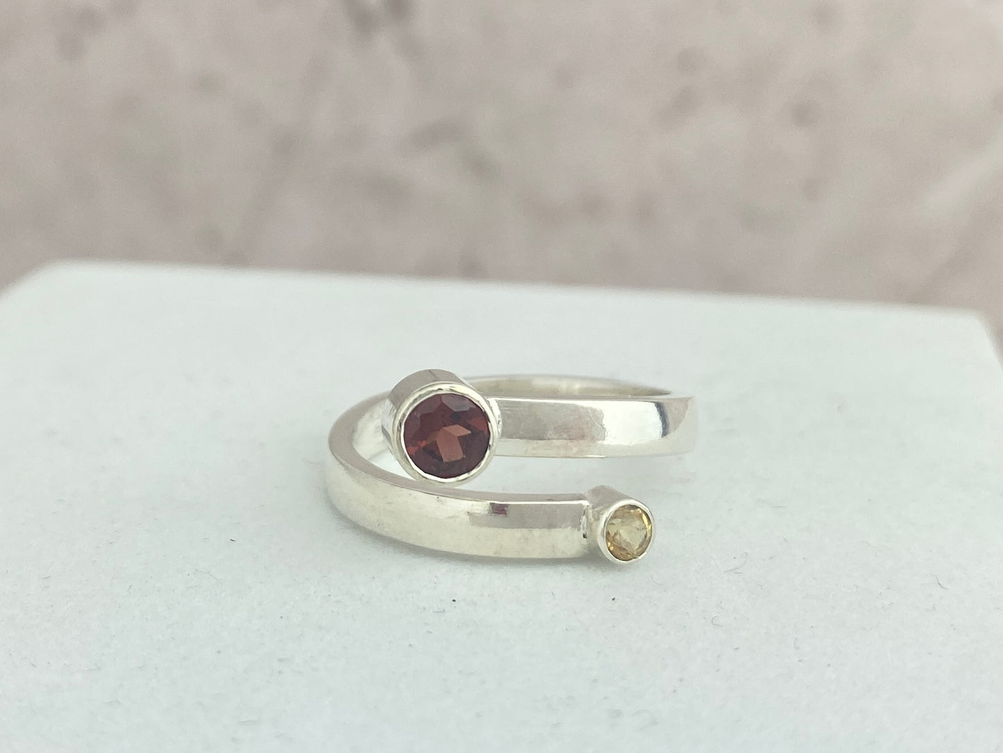 Silver ring with a deep red garnet gemstone and a citrine gemstone on a white surface.