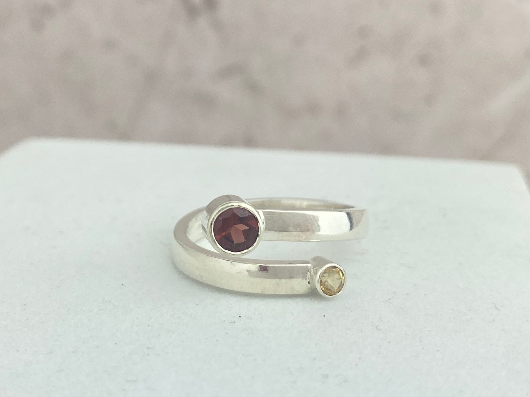 Silver ring with a deep red garnet gemstone and a citrine gemstone on a white surface.