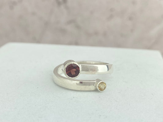 Silver ring with a deep red garnet gemstone and a citrine gemstone on a white surface.