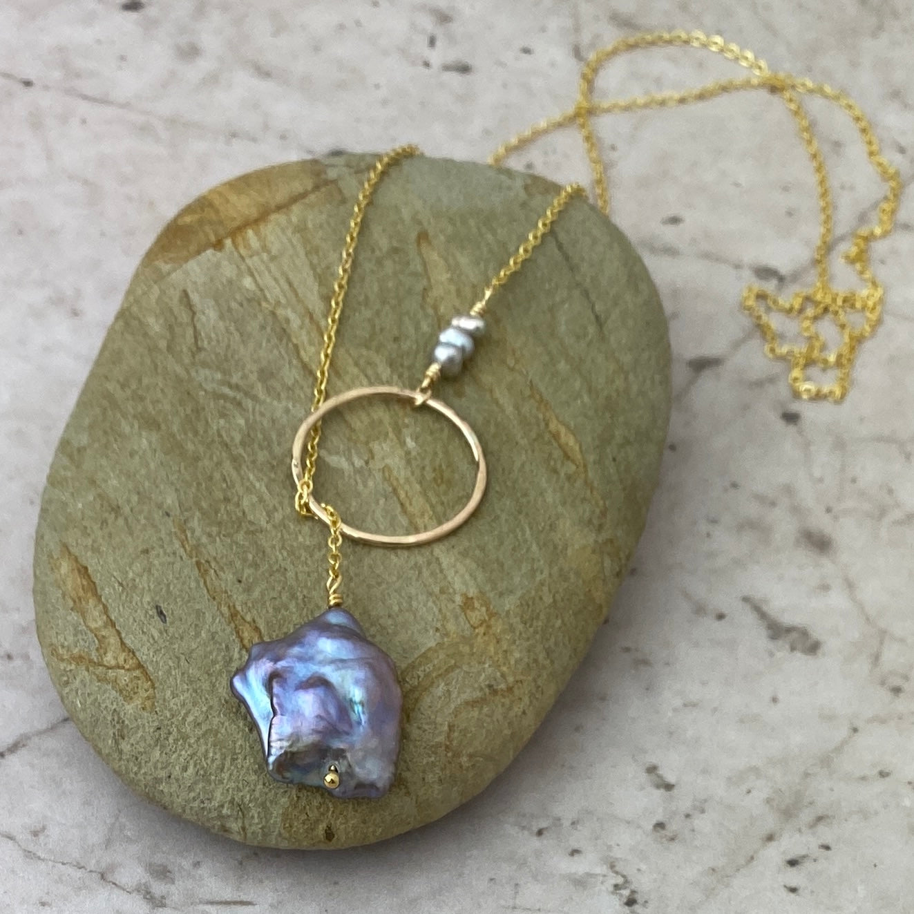 Gold necklace with a silver pearl pendant on a stone surface